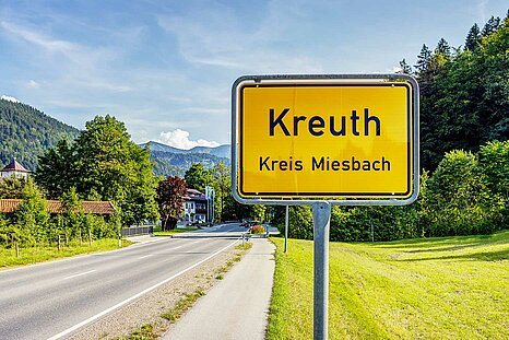 Das Bild zeigt das Verkehrsschild von Kreuth mit Blick auf die Berge im Hintergrund