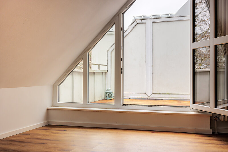 Vorher: leeres Dachgeschosszimmer mit Schrägfenster, Holzboden und Blick auf die Dachterrasse