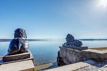 Zu sehen sind Löwenstatuen vor einem See