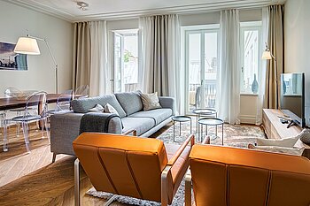 Zu sehen ist ein luxuriös eingerichtetes Wohnzimmer, mit Sitzgruppe, Fernseher und Fensterfront