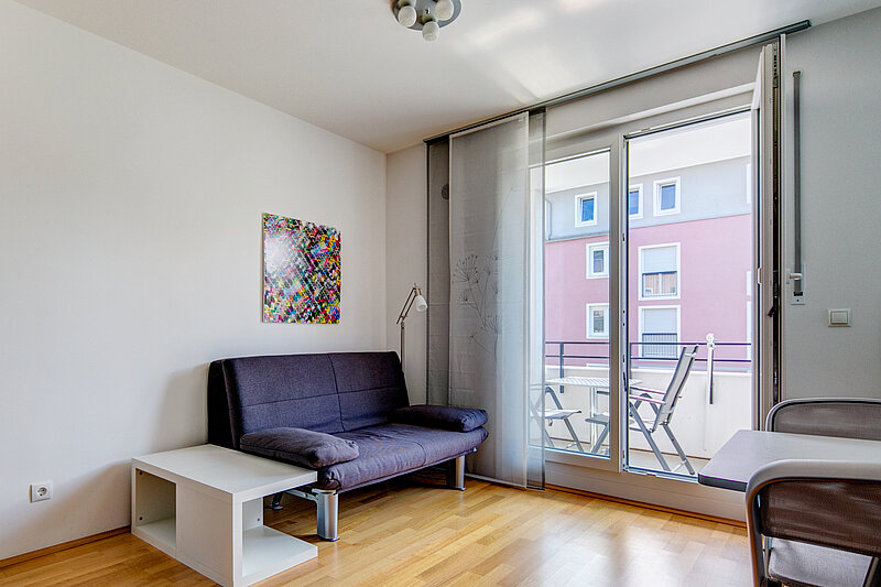 Wohnraum vorher Zu sehen ist ein praktisches Schlafsofa und ein kleiner Esstisch für zwei Personen.