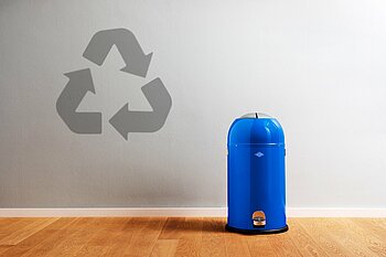 Blaue Mülltonner vor grauer Wand mit Recyclingsymbol