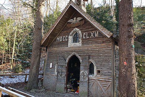 Zu sehen ist ein Holzhaus "Marienklause" umgeben von Bäumen