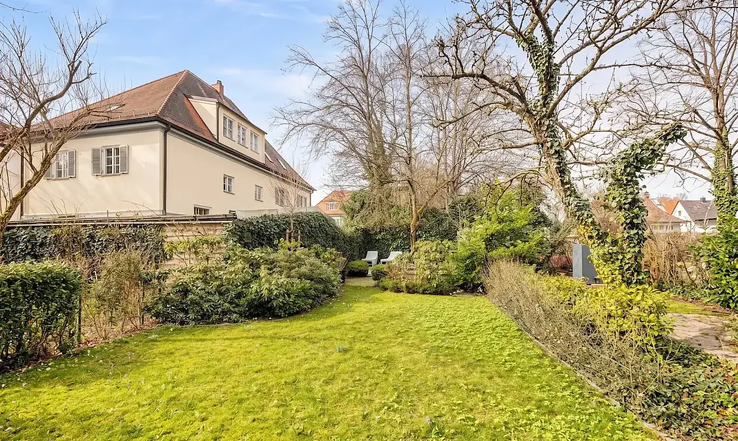 Passender Alttext für diese Gartenaufnahme auf der Seite „Grundstück verkaufen München":  Alttext: Gepflegter Garten eines klassischen Münchner Wohnhauses mit weitläufiger Rasenfläche, umgeben von Sträuchern und altem Baumbestand — ein repräsentatives Grundstück in gehobener Münchner Wohnlage
