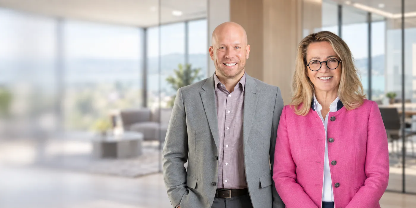 Petra und Alexander, Immobilienmakler am Tegernsee, lächeln in einem hellen Wohnraum